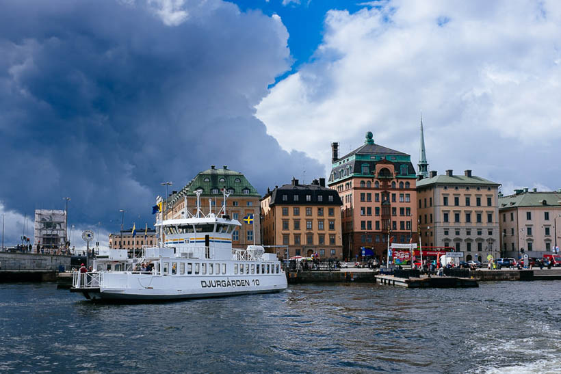 A ferry boat docked at Djurgården, an island in Stockholm, overlooked by dark clouds on an otherwise sunny day.