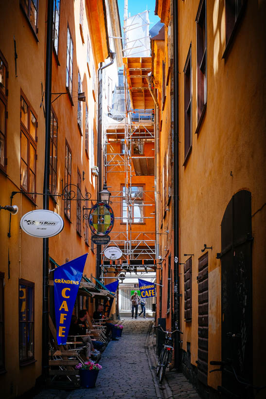 A narrow back street at noon in Gamla Stan in Stockholm, with tall orange painted buildings and scaffolding for a renovation in progress.