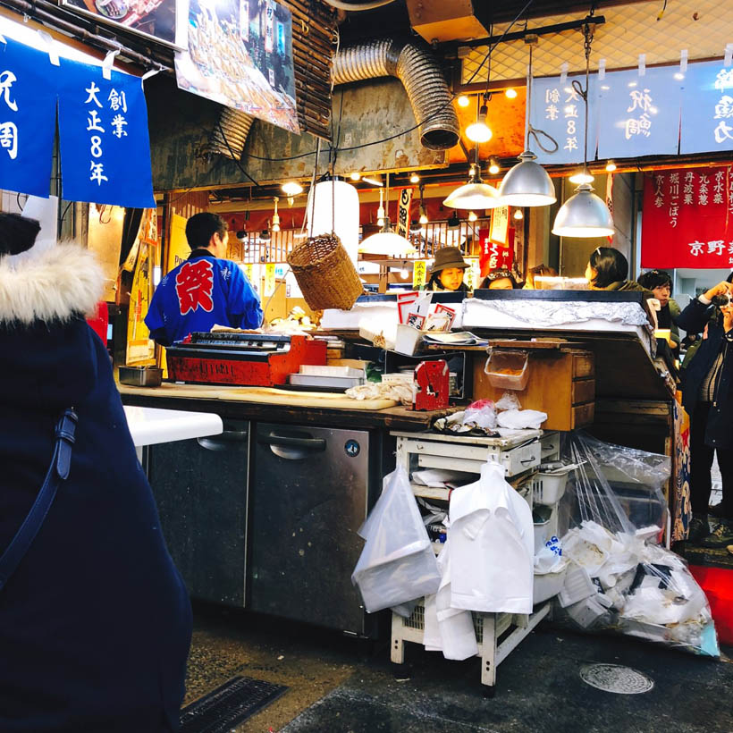 A food stall in Nishiki Market in Kyoto, Japan, selling grilled eel, as seen from inside.