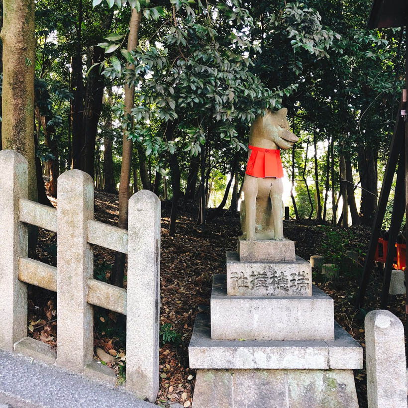 A fox statue with a red yodarekake around its neck at Fushimi Inari Shrine in Kyoto, Japan.