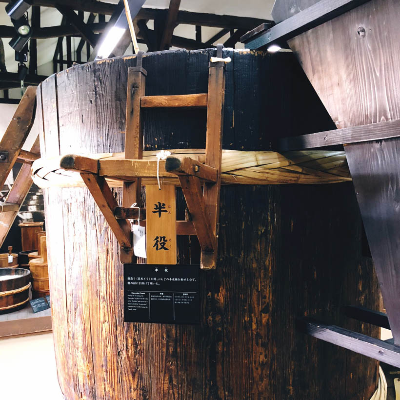 A large wooden steaming bowl used in the sake brewing process with a stand (labeled Han-yaku) attached to it at the Gekkeikan Okura Sake Museum in Kyoto, Japan.