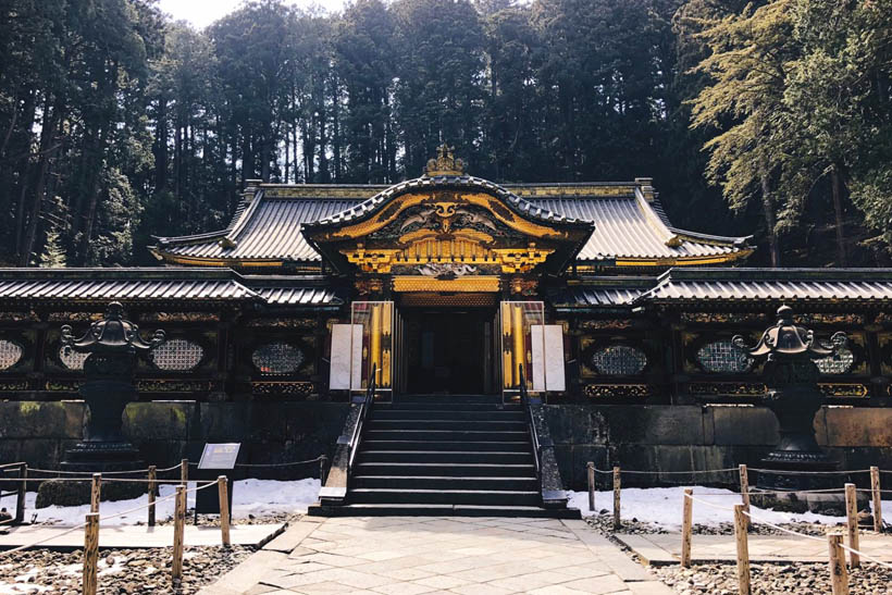 The Taiyuinbyo Shrine in Nikko, Japan, a black woorden building decorated with gold, on top of a hill and surrounded by trees.