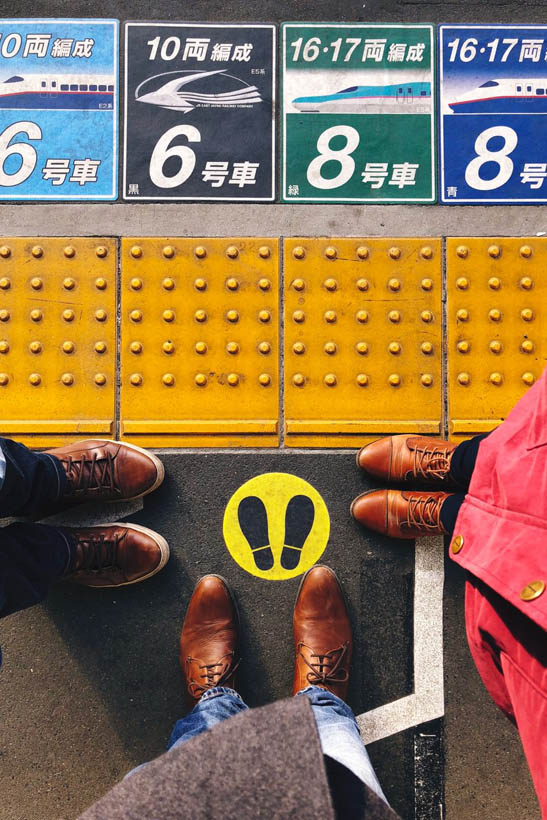 The feet of three travellers at a waiting sign at the Shinkansen train track at Utsonomiya, waiting for the train to Tokyo, Japan.