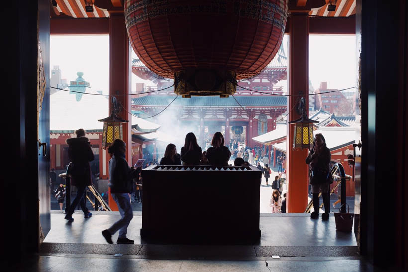 People praying with incense burning behind them at the main building of the Senso-ji temple in Asakusa in Tokyo, Japan.